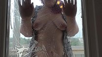 Una ragazza grassoccia in una camicia sbottonata e in mutande lava la finestra e scuote belle tette.