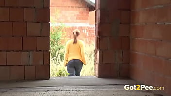Blonde junge Frau pisst auf eine Baustelle, um ihre Verzweiflung beim Pinkeln zu lindern